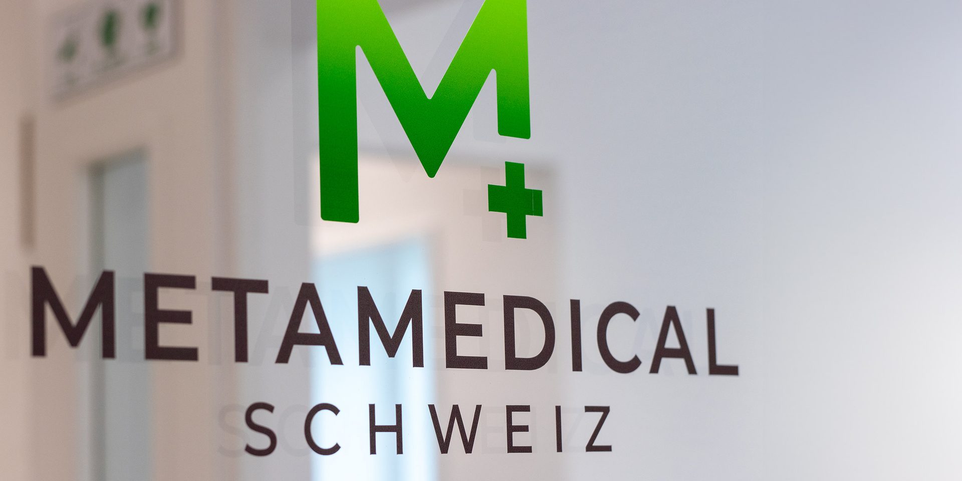 Metamedical-Schweiz-Logo auf der Glastür am Praxiseingang, dahinter der helle Innenbereich
